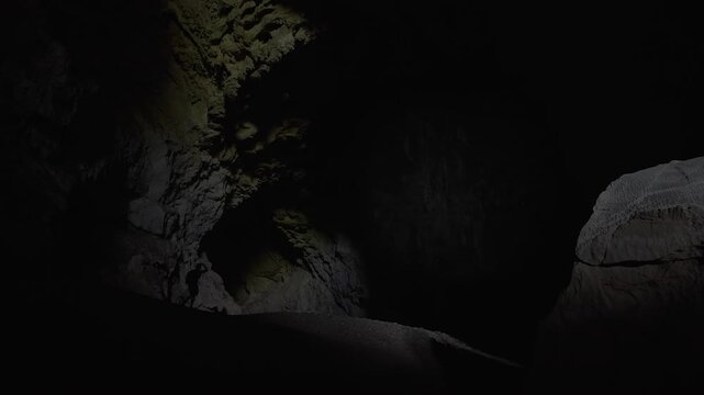 Static shot of Nam Non cave, with a man looking around at the high ceiling before walking out of frame.
