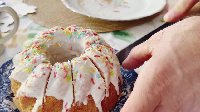 Close-up of slicing traditional Easter cake with white glaze and colorful sprinkles during family celebration.