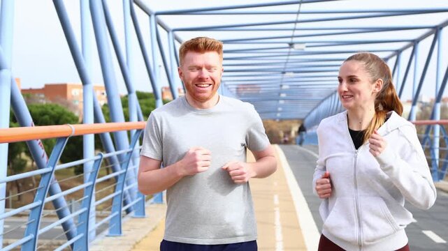 Happy young couple jogging together on a modern city bridge