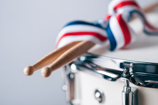 Drumsticks rest on a snare drum decorated with a red white and blue ribbon tie.