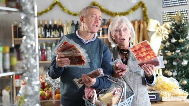 Elderly couple is looking at meat delicacies in store. Market visitors choose from several types, consult and consider choose vacuumed hamon and dried smoked sausage. 