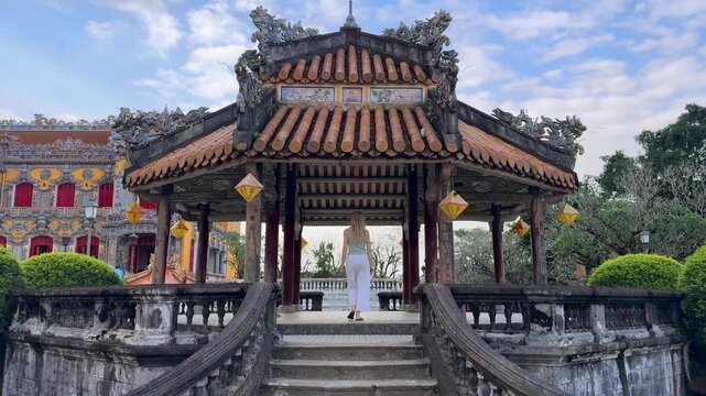 Woman walking up stairs toward traditional pavilion in the Imperial City, Hue, Vietnam. Scenic cultural setting with historic architecture, lanterns, and symmetrical design.
