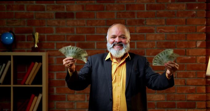 Indian senior businessman flaunting a fan of five hundred rupee notes to the camera with joy and success while standing against a red brick wall in a cozy office with professional moody lighting