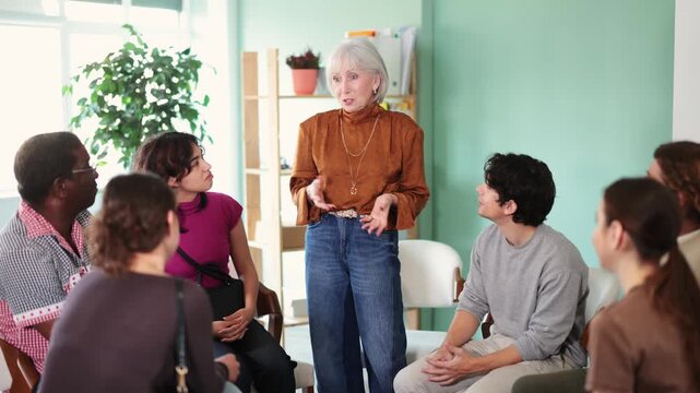 Friendly and calm senior female psychotherapist or facilitator leading group therapy session with women and men of different ages and nationalities . High quality 4k footage