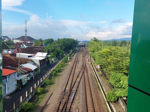 Parallel railway tracks leading toward a station surrounded by houses and greenery.