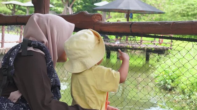 Woman at a zoo with child, observing animals behind a fence. Perfect for illustrating family outings, wildlife conservation, and education.