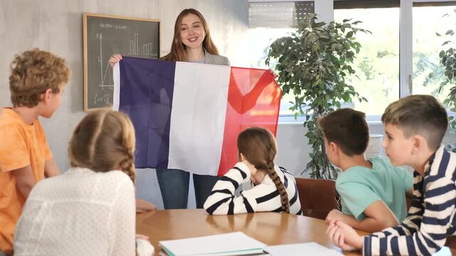 Geography lesson in school class - teacher talks about France, holding a flag in his hands. High quality 4k footage
