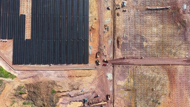 Drone aerial of solar farm construction showing panels, machinery, and installation on cleared earth.