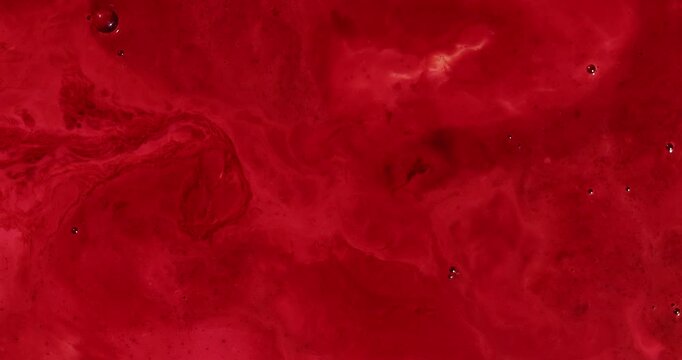 Red liquid swirls and moves extremely slowly as bubbles move and pop.