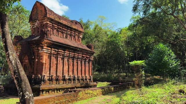 Ancient Cham Hindu temple tower at My Son Sanctuary near Hoi An, Vietnam. Red brick ruins surrounded by lush jungle forest under blue sky, UNESCO World Heritage Site.