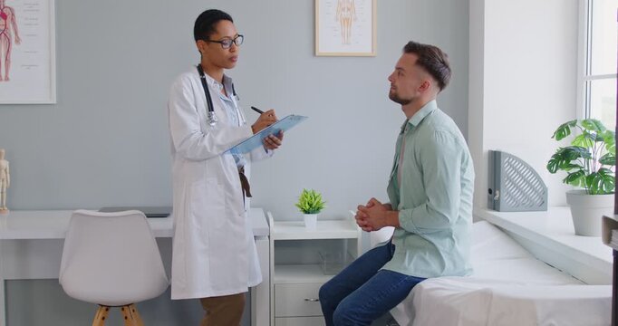 Doctor and man patient in clinic consultation. Physician explains medical options and diagnosis during routine appointment in examination room. Healthcare, exam and medicine concept. 