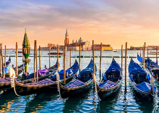 row of parked venetian gondola boats in Grand canal of Venice. Beautiful sunset or sunrise landscape with gondolas in blue water of Venice.