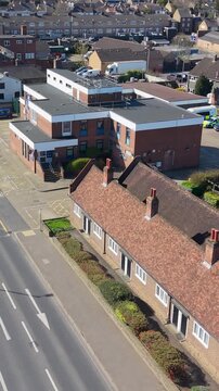 Cheshunt police station drone vertical ascent establishing shot over Hertfordshire suburb with main road, almshouses, bus lane marking, rooftops, traffic and neighborhood buildings in daylight.