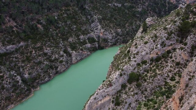 Cinematic 4K FPV-style drone orbit around a steep limestone cliff. High-speed aerial maneuver over the turquoise J&uacute;car River canyon and Mediterranean pine forests in Castilla-La Mancha, Spain.