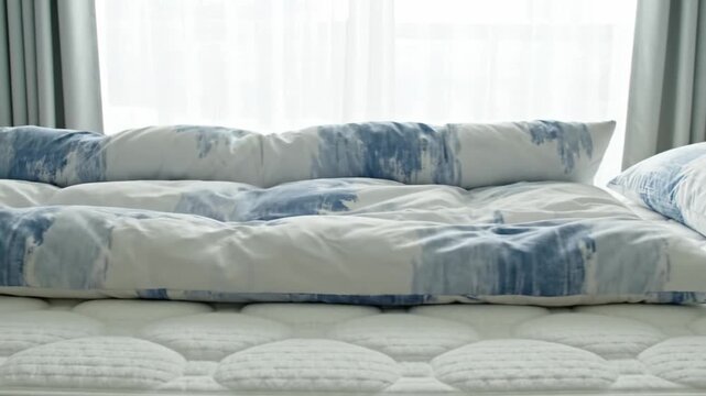 A person spreads a blue and white patterned duvet over a white quilted mattress in a bright room. Morning routine and home comfort. Ideal for lifestyle and interior design content.