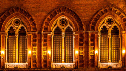Obraz premium old yellow facade of house with three brown vintage windows in retro gothic italian european style. Night italian architecture.