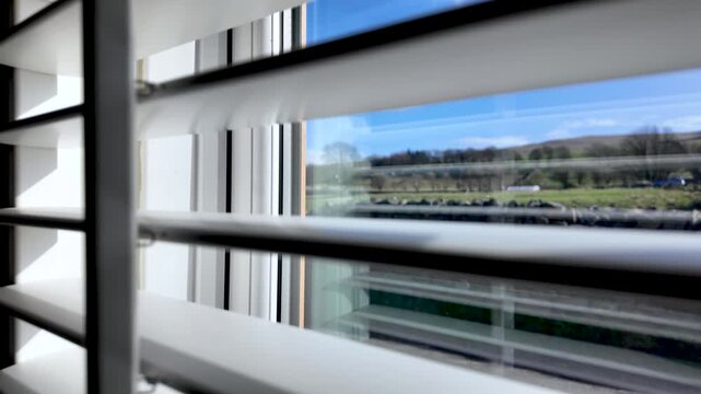 White window shutters showing a peaceful rural landscape and blue sky from indoors