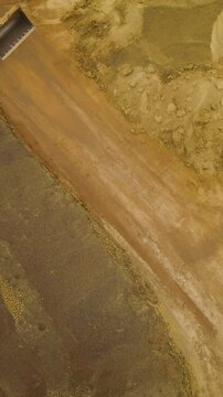 High angle aerial shot of a yellow front end loader moving across a sandy construction site or quarry, suitable for industrial and civil engineering projects.