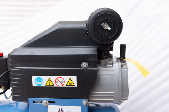 Side view of a direct-drive piston air compressor pump motor with a black protective casing, safety warning labels, and a round intake filter element.