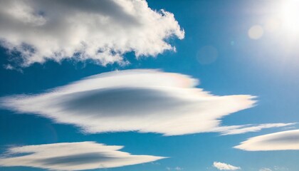 Obraz premium Dominating lenticular cloud hovering in deep blue sky with sun lens flares and cumulus fragments