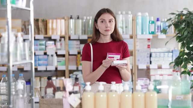 Young woman buyer chooses box of paracetamol tablets in pharmacy
