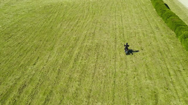 Aerial View of a Motorcyclist Riding Across a Green Grass Field