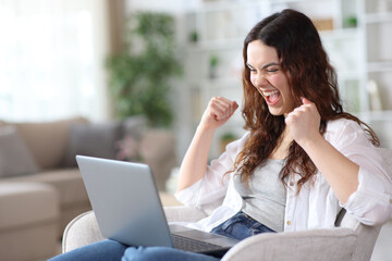 Excited young woman checking good news on laptop