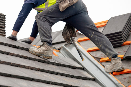 Workers repair a roof on a cloudy day in a construction area using tools and materials