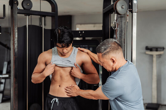 Young Asian man does body composition check at the gym, guided by a trainer assessing abdominal definition and body fat percentage for fitness progress.