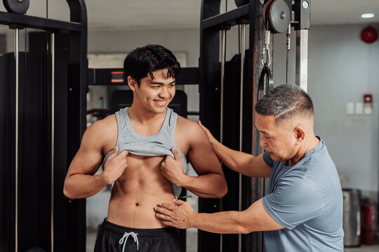 Young Asian man does body composition check at the gym, guided by a trainer assessing abdominal definition and body fat percentage for fitness progress. Happy with current pace.