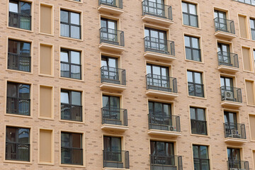 Fototapeta premium Modern apartment building with curved, textured facade. Balconies feature black railings and glass doors. Warm beige tones contrast with dark window frames