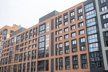 Fototapeta premium Modern apartment building with orange and gray facade. Large windows reflect surrounding urban environment. Structured design suggests contemporary urban living. Ideal for architectural, real estate