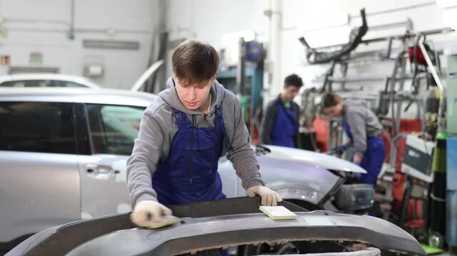 Guy worker removes dents on cars exterior, restores vehicle to its original form. Male auto mechanic polishes bumper, eliminating deformations, hiding flaws. Business hour 24 service coverage.