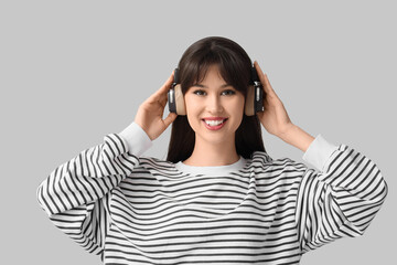 Fototapeta premium Smiling young woman in headphones on light background