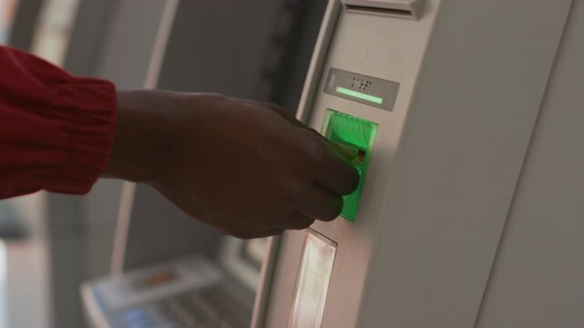 Darkskinned male engaging with outdoor ATM machine, Closeup view of man using bank card at kiosk in city environment
