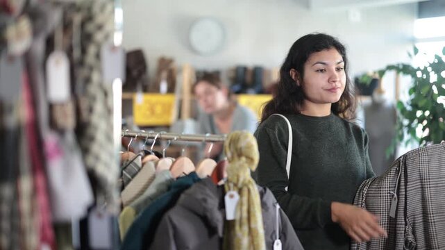 Latina woman in warm sweater looking at pants for autumn and winter in a clothing store. Customer stands on sale in a clothing store