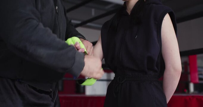 Close-up hands of a trainer applies protective wraps to a young female boxer's hands training, providing protection and support to her wrists and knuckles in preparation for intense boxing training.