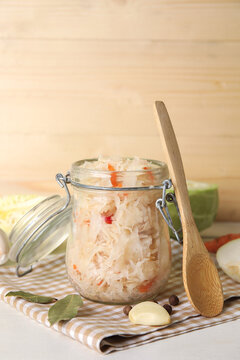 Tasty sauerkraut in jar with ingredients on wooden background