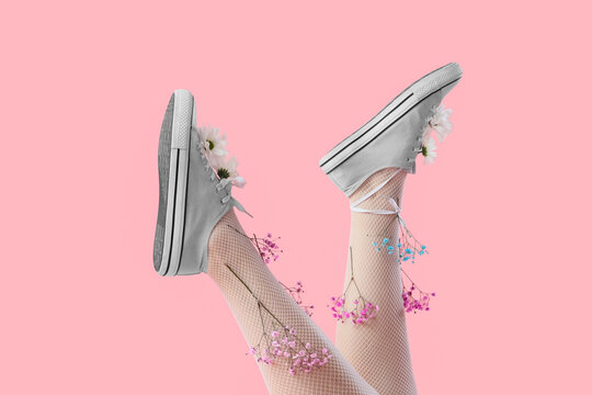 Female legs in tights and sneakers with gypsophila flowers on pink background