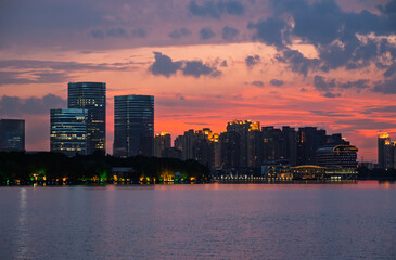 Naklejka premium Vibrant sunset hues paint the sky above a contemporary city skyline visible from across a calm lake