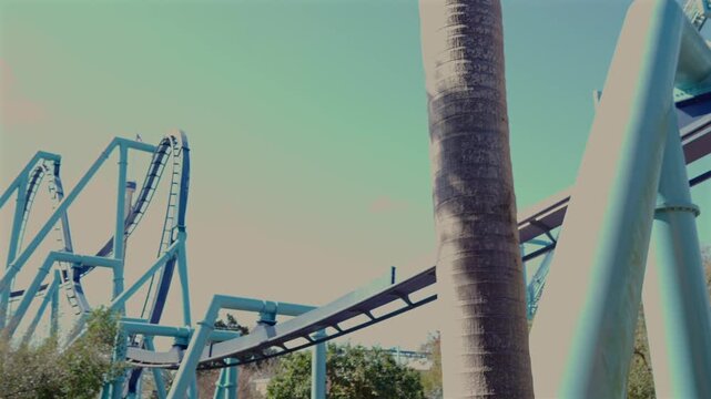 Roller coaster track curving above yellow flowering tree against clear blue sky in amusement park