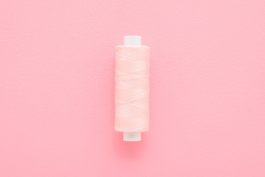 New pink thread spool on light pink table background. Pastel color. Closeup. Top down view.