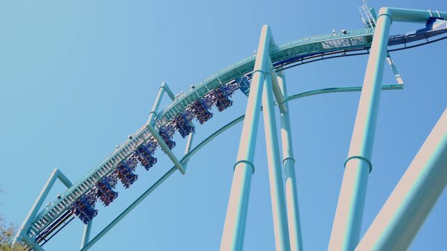 Inverted roller coaster train with passengers moving along high track against clear blue sky in amusement park