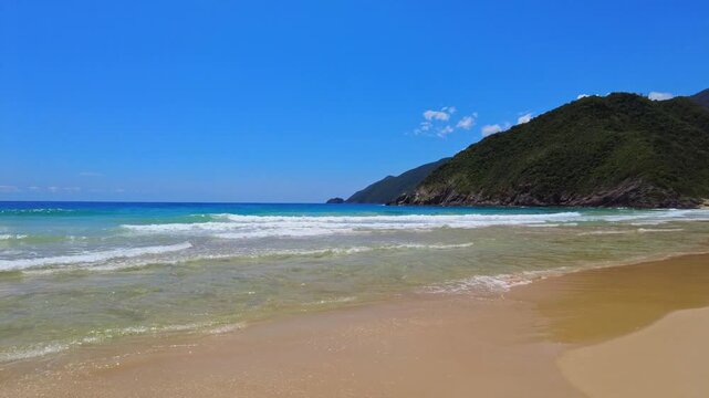Panoramic view of the expansive beach at Choroni, with crystal-clear waters and green mountains on either side, on a sunny day, Aragua, Venezuela