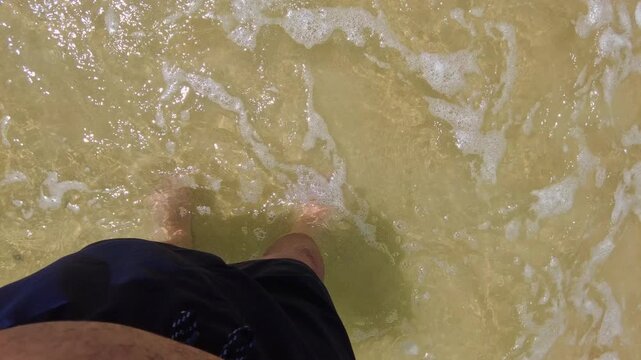 A static POV shot of the large beach at Choroni, with feet submerged in its greenish, crystal-clear waters in Aragua, Venezuela