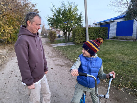 father proudly watching son riding bicycle during evening walk on rural road countryside family bonding parenting support and childhood independence concept