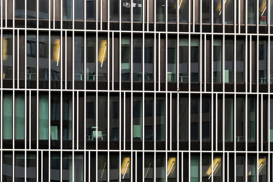 Night lights behind modern office windows and vertical fins on building facade form a striking pattern with architecture mood and abstract texture