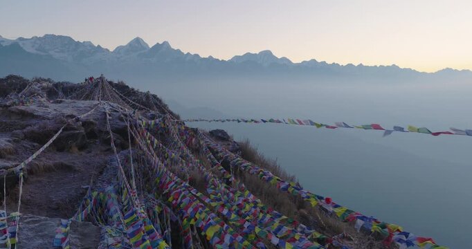 Aerial drone shot capturing a golden sunrise over the Buddhist Ama Yangri viewpoint in Helambu Nepal with prayer flags fluttering against the Langtang and Gauri Shankar mountain ranges.