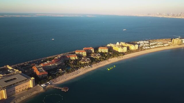 Drone ascending and pulling back over Palm Jumeirah in Dubai showing villas, sea, boats and distant marina at sunset.