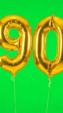 Golden number balloons celebrating ninetieth anniversary on green backdrop